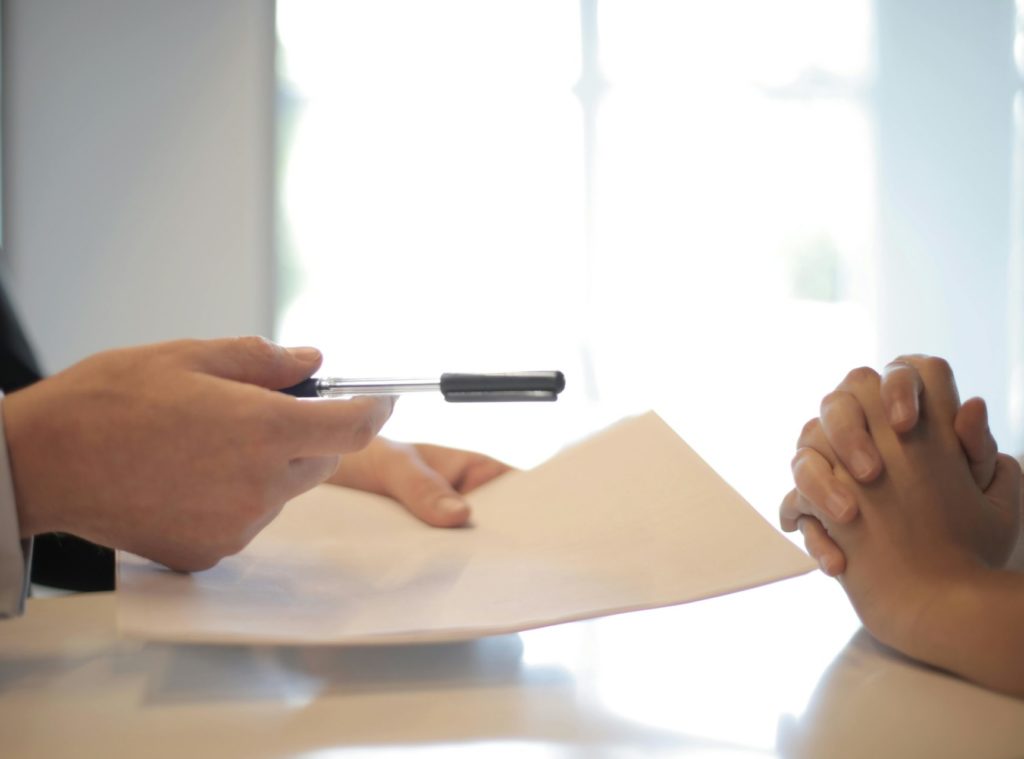 A person is handing over a pen to another individual who appears to be awaiting a signature or action related to the document on the table.