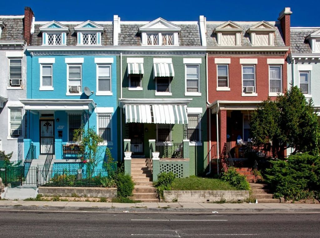 A row of colorful, neatly aligned two-story townhouses with contrasting awnings under a clear blue sky.