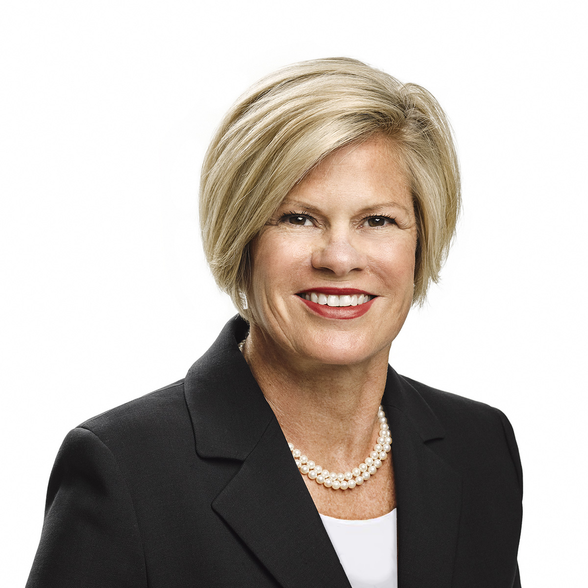 A professional portrait of an individual with a confident smile, wearing a black blazer and a pearl necklace against a white background.