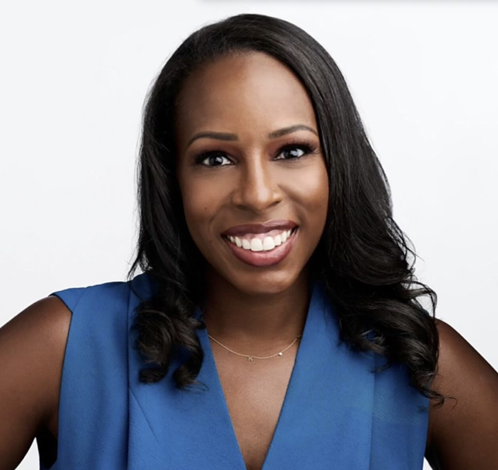 A smiling individual with long black hair wearing a blue top is posing against a white background.