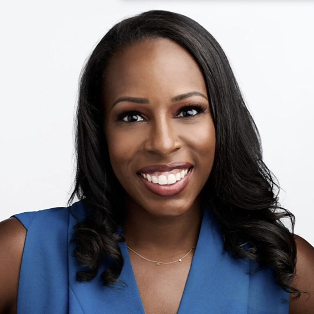 A smiling individual with long black hair wearing a blue top is posing against a white background.