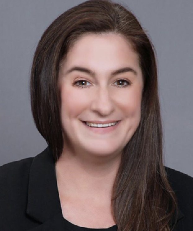 A person is smiling at the camera, wearing professional attire against a grey backdrop.