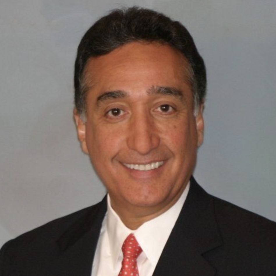 A smiling individual wearing a suit with a red tie poses against a plain background.