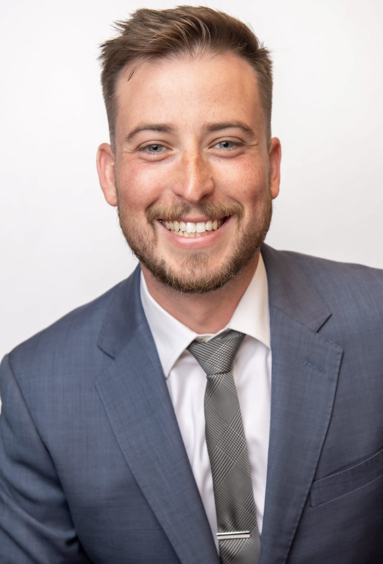 A smiling individual with a beard is wearing a suit and tie.