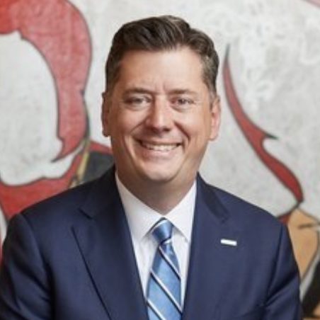 A person is smiling in front of an artwork with a blue suit and a striped tie.