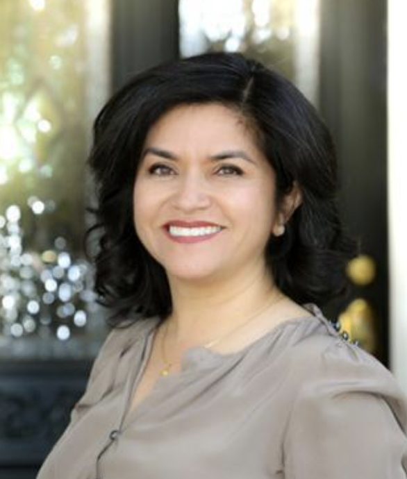 A person with shoulder-length dark hair is smiling in front of a blurred background.