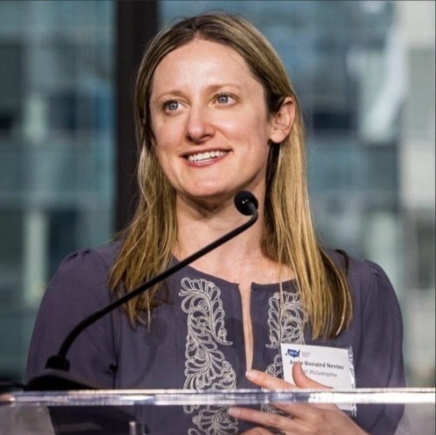 A person is smiling while standing at a podium with a microphone and wearing a name tag.