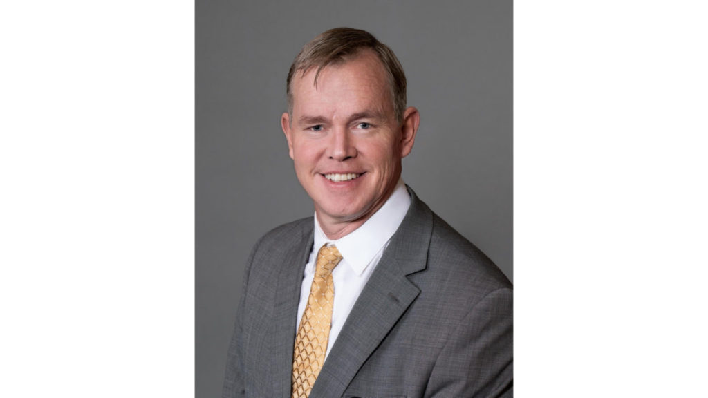 A person is smiling for a professional headshot, donning a suit and a patterned tie.