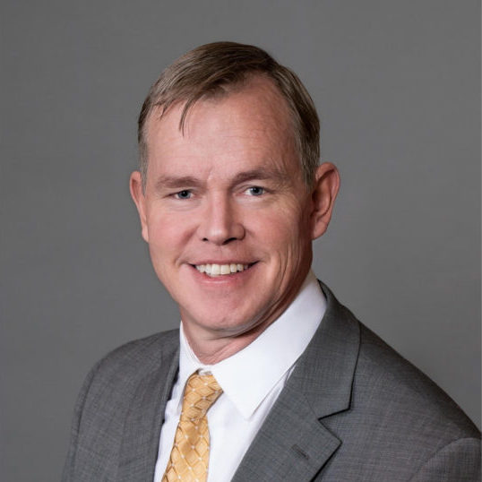 A person is smiling for a professional headshot, donning a suit and a patterned tie.