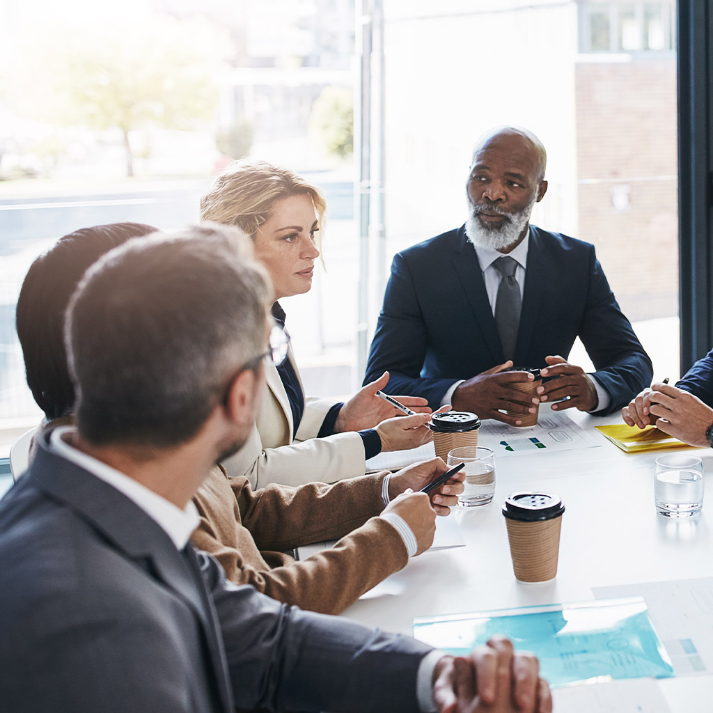 Professionals are engaged in a focused discussion around a table with documents and coffee cups.