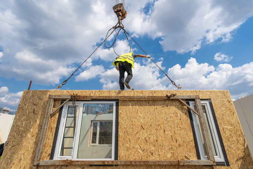 A construction worker stands on top of a wall that was built in a factory.