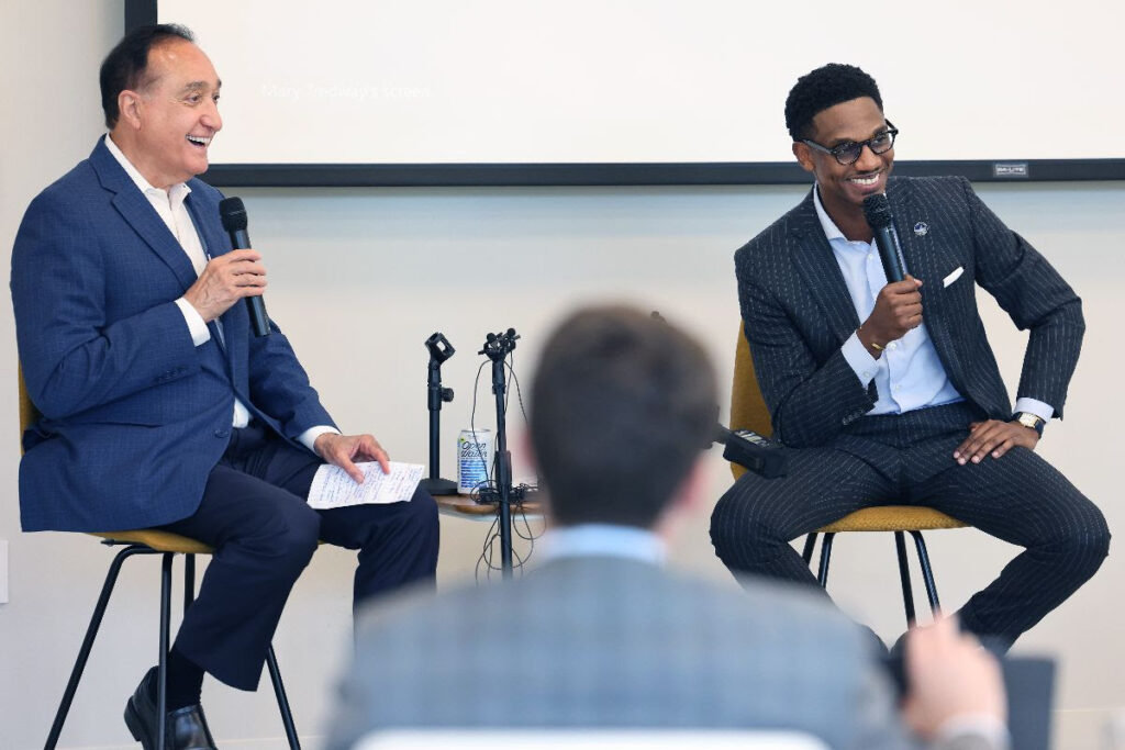 Mayor Justin M. Bibb and former HUD Secretary Henry Cisneros, a Task Force member, sit on high-top chairs holding microphones as they talk to a group of housing leaders and practitioners.